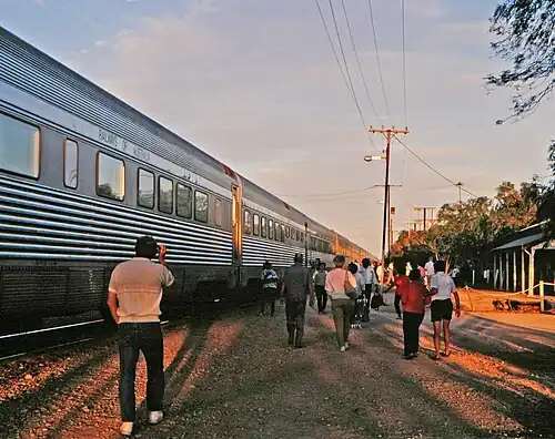 People strolling alongside stainless steel passenger cars with "Railways of Australia" above the windows