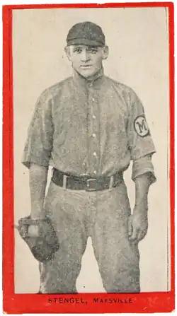 a young man in an old-style baseball uniform wears a glove and stares at the camera