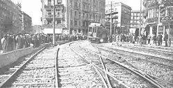 Black and white photograph from an urban rail area with three tracks. On the background, a wagon can be seen. On both sides of the track area, white men stand.