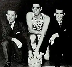 Babe McCarthy, Joe Dan Gold, and Jerry Simmons each take a knee with their hands on a basketball.