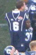 Connecticut Huskies football uniform with number 6 held up by another uniformed player on the sideline