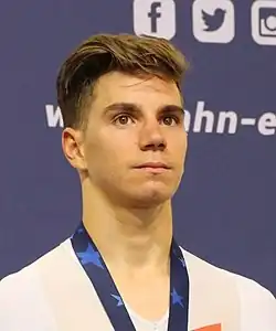 Oliveira during a press conference in 2017 with a silver medal. He is a young, white man with brown hair, wearing a white cycling suit.