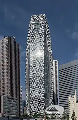 Ground-level view of a blue, glass high-rise. Two opposite sides of the building curve inward until meeting at the top; these sides also have many white stripes haphazardly strewn across them.