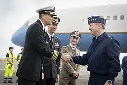 Two men shaking hands, with a plane in the background