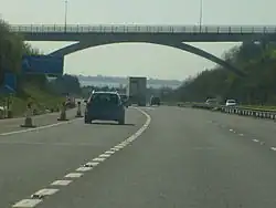 multi-carriageway road with vehicles passing under an elevated roadway and distant view of sea beyond