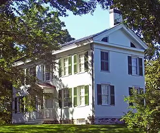 A white house with green shutters and gray roof in the middle of some trees