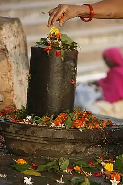 A woman spreading flowers over a lingam, a symbol of the Hindu god Shiva