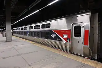 A silver railroad car with a blue stripe over the windows. At one end, an angular red shape covers the stripe
