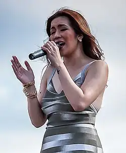 A photo of Quinto singing to a hand-held microphone with her eyes closed