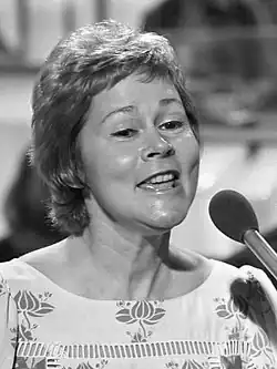 A black-and-white image of a woman with short hair singing into a microphone.