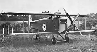 Three-quarter front view of biplane with four-bladed propeller, parked in a field