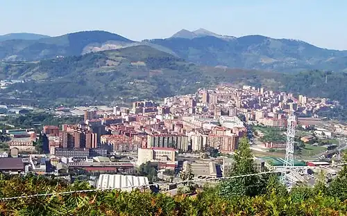 Aerial view of the city of Basauri with green mountains in the background and large powerlines in the foreground