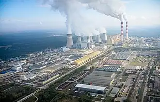 Aerial view of the Belchatow Power Station site, with smoke coming from its smokestacks, and surrounding buildings.