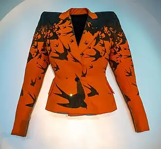 An orange jacket printed with black birds, laid flat on a surface