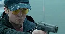 Teenager pointing a gun and wearing a hat and yellow glasses