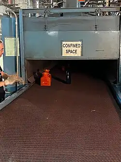 glassware at end of conveyer being watched by worker wearing gloves