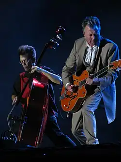 Brian Setzer, in a gray suit, strumming a guitar