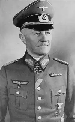 A man wearing a peaked cap, military uniform with an Iron Cross displayed at the front of his uniform collar.