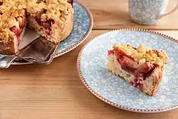 Slice of plum cake on a china plate; the rest of the cake is in the background