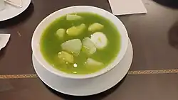 a bowl of green coloured soup with light-coloured vegetables
