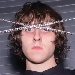 A photo of the artist's face, with two metal chains crossed in front of his browline and partially obscuring his eyes.