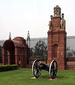 An iron fence interspersed with stone columns. Alongside the column is a gateway-like red sandstone aedicule with a barrel-vaulted roof. They are tall enough to provide shade for a soldier on horseback.