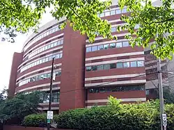 A circular, six-story brick building with decorative white concrete stripes above and below lines of adjacent square windows that encircle most of each level