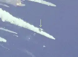 A trapezoidal gray section of the shuttle among several plumes of smoke and vapor against the blue sky