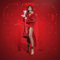 Charli XCX wears a red quilted coat and high heels in front of a red background. She holds a white rose.