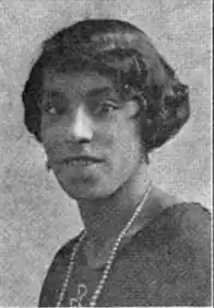 A young African-American woman, with dark hair cut into a 1920s bob, wearing drop earrings and a strand of pearls.
