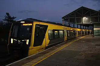 A Merseyrail train painted with a black front and grey-yellow sides. It is preparing to depart from Chester station.
