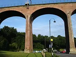 A large arch in red brick, part of a larger structure, with sky and trees visible through it