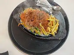 Chicken sizzler is served on high temperature in heavy wood utensils.