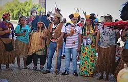 Indigenous protesters are standing wearing traditional garments along with "common" clothes