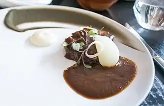 A slice of meat covered with a sauce, onion, and herbs.