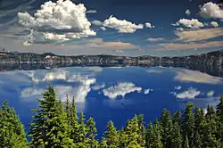 The water of Crater Lake can be seen above a forested area in the foreground.