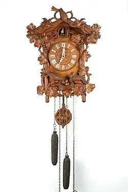 Wood carvings composed of a vine with grapes, a bird on top, nest with eggs and parents and a matching pendulum bob (Deutsches Uhrenmuseum)