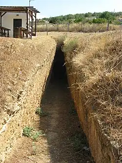 The passageway of a chamber tomb: a narrow rectangular cutting, sloping downwards from the viewer.