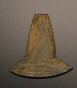 Photo of a metallic object shaped as an axe-head. It has brown irregular surface and rests on a black plate.