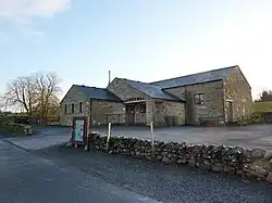 A sandstone building set in a small car park with a low sandstone wall surrounding the car park