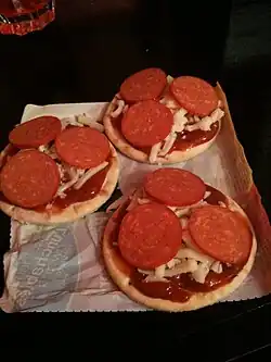 Three "pizzas," consisting of a base, tomato sauce, shredded cheese, and three small slices of pepperoni each, all sitting atop Part of the meal's wrapper.