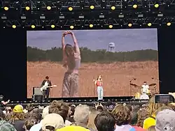 Anhedönia and a band performing on a stage in front of a screen showing visuals of herself in a field