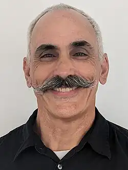 Evan Prodromou smiling and facing the camera with his back against a white background