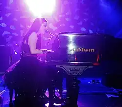 Young woman with long, dark hair singing and playing piano onstage