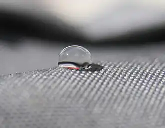 side view of a drop of water on a gray cloth. Looks like about a 120 degree angle.
