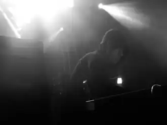 Justin Broadrick in a hoodie holding a guitar next to a Marshall amplifier