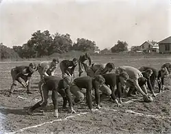 A football team crouching in preparation for a snap on a dirt field