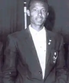 black-and-white image of Turab Ali wearing a light-coloured shirt and a dark suit, grinning directly at camera