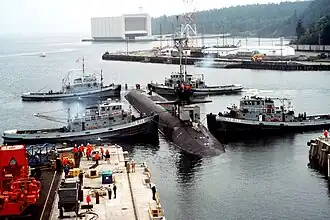 Naval Submarine Base Bangor with tug Mishawaka (rear left) and three other Natick-class tugs guiding the USS Ohio (SSGN-726) out of dry dock at Delta Pier