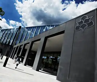 Manchester Metropolitan University Business School front entrance. The main front doors are pictured with the University logo prominent at the front of the image.